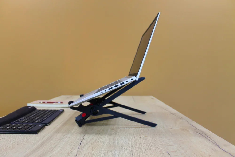 Roost V3 folding stand supporting a laptop beside an external keyboard on a wood desk