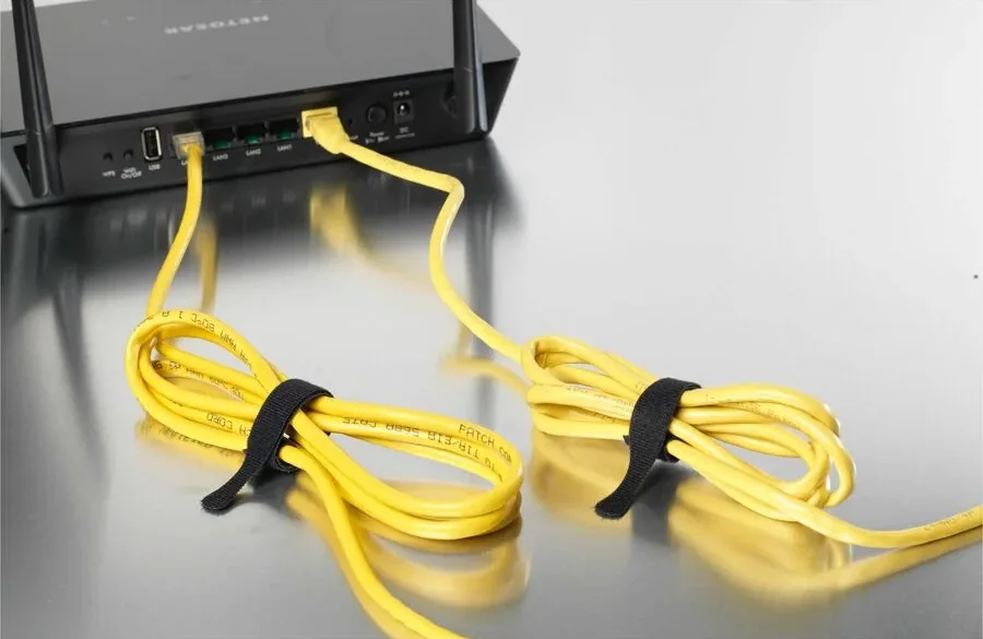 Black VELCRO Brand ONE-WRAP ties securing two coiled yellow network cables beside a router